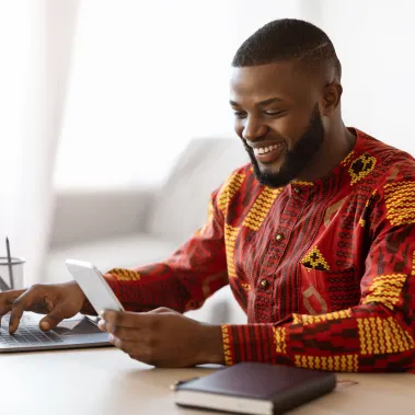 Man smiling and using laptop and cell phone