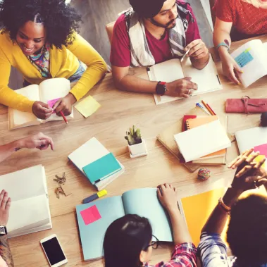 People with books and pens working and talking around a table