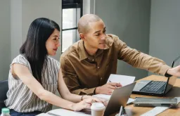 Man and woman sitting at desk in front of computer screen